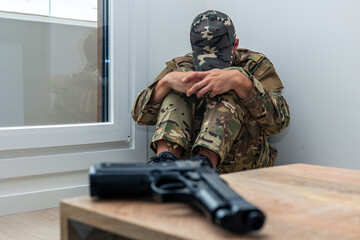 Depressed soldier sitting on floor suffering post-traumatic stress disorder near gun