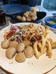 Close-up view of a plate filled with fried seafood, crispy potatoes, and a vibrant salad.