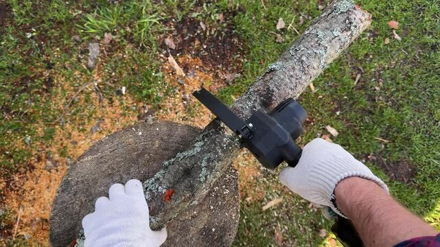 Gardener cutting wood log with portable reciprocating saw outdoors