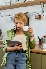 Senior woman enjoying coffee while reading on a tablet in a cozy kitchen setting