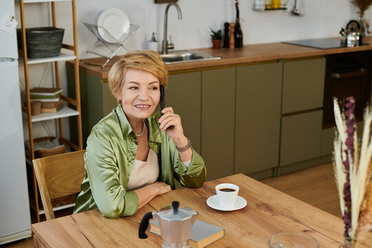 Senior woman enjoys a warm coffee moment while having a cheerful phone conversation at home