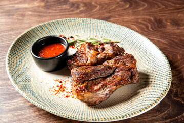 Succulent grilled beef ribs served on a textured plate with a side of spicy dipping sauce and garnished with fresh rosemary, creating an inviting and hearty meal.