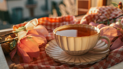 Vintage teacup with tea on a wooden tray by a window, surrounded by pink flowers and soft sunlight, with a warm and peaceful morning atmosphere