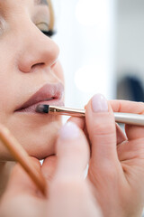 close up Professional lips Makeup, beautician applies lipstick, Beautiful woman face, Hand of make-up master in beauty salon, painting lips, Make up in process 