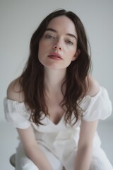 Fototapeta premium Woman with long brown hair is sitting on a chair and wearing a white dress