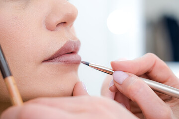 close up Professional lips Makeup, beautician applies lipstick, Beautiful woman face, Hand of make-up master in beauty salon, painting lips, Make up in process 