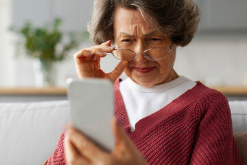 Confused elderly woman in eyeglasses squinting eyes, having problems with vision and trying to read...