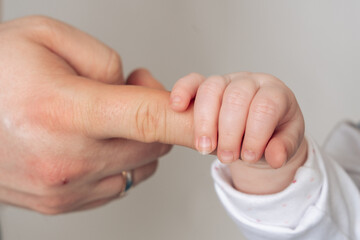 Close-up of a babys tiny hand gently gripping an adult finger, symbolizing trust, care, and...