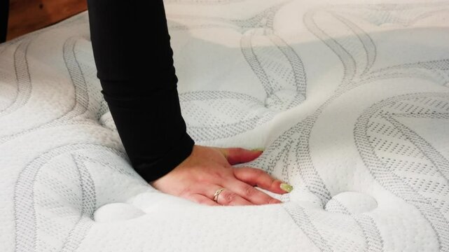 Woman&rsquo;s hand with ring presses into white mattress to feel softness and support