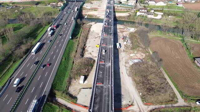 High-resolution aerial footage showing a busy Italian highway with dense traffic alongside an active construction site for a high-speed rail (TAV) project.