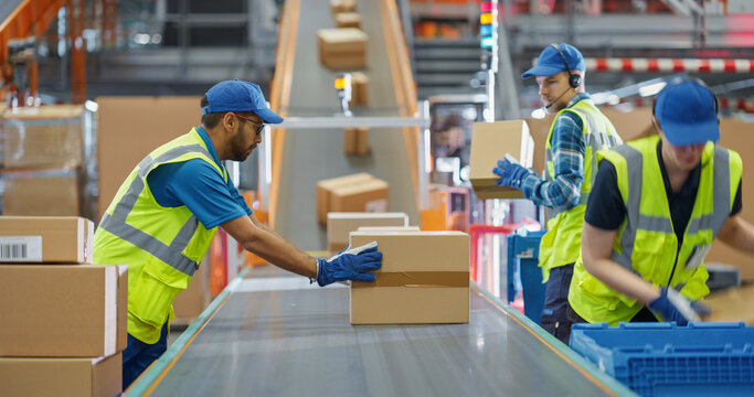 Workers in High-Visibility Vests Redirect Packages Along a System of Conveyor Belts in a Distribution Hub. Male and Female Working in Large-Scale Retail E-Commerce Operation or Logistics Service