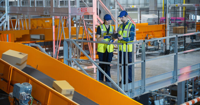 Portrait of a Female and Male Technicians with a Tablet Computer Monitoring Automated Conveyor Belt with Packages in a Logistics Warehouse. Modern Fulfillment Center with Internet Shop Orders - Powered by Adobe