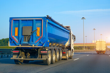 Truck huge blue dump trailer heavy bulk cargo drives fast along the highway, rear view