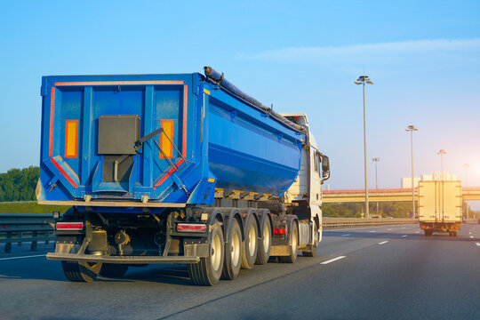 Truck huge blue dump trailer heavy bulk cargo drives fast along the highway, rear view