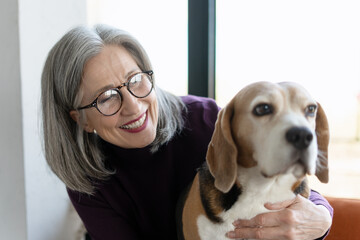 Smiling senior woman hugging beagle dog at home