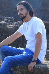 Confident young man with a casual style sitting in a green park on a sunny day