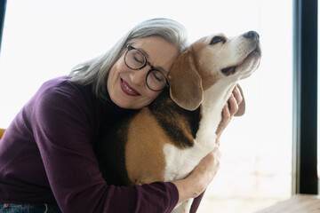 Senior woman embracing beagle dog with closed eyes and smiling