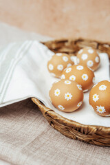 Hand-painted Easter eggs with daisy flowers in a wicker basket. Rustic spring composition for festive celebration.