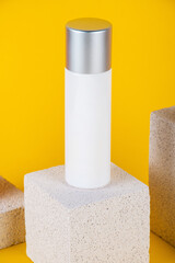 Cosmetic product in tube, bottle, lotion or serum with stylish props on yellow background. 