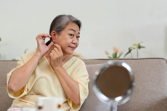 Beauty and Age Diversity. A senior woman putting on earrings in a comfortable living space. - Powered by Adobe