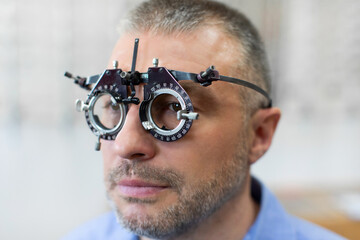 Middle aged man wearing optometrist trial frame to select glasses for vision treatment, doing eye...