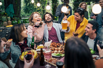 Group of friends laughing and toasting at outdoor dinner party with lights and food