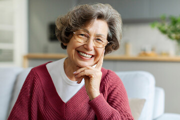 Portrait of delightful senior woman, sitting on couch and smiling at camera, creating heartwarming moment of relaxation at home