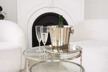 Stylish living room features metallic ice bucket holding champagne. Two elegant glasses sit on a glass table, ready for a festive occasion in modern white interior background