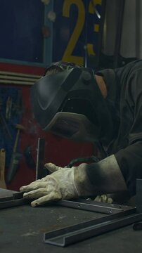 Vertical video of Welder operator wearing personal protective equipment working in the welding workshop, fusing steel parts together, using MIG welding proccess medium shot. Metal industry concepts.
