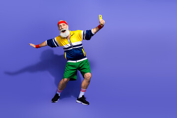 Obraz premium Elderly man dressed in vibrant retro sportswear posing energetically on a purple background