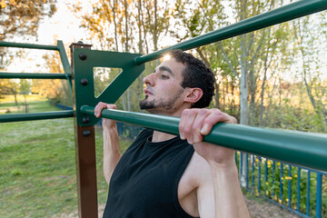 Athletic man doing pull-up on green outdoor bar at sunset, demonstrating upper body strength,...
