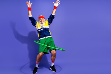 Elderly Cheerful man practicing hula hoop exercise in retro 90s attire on purple background