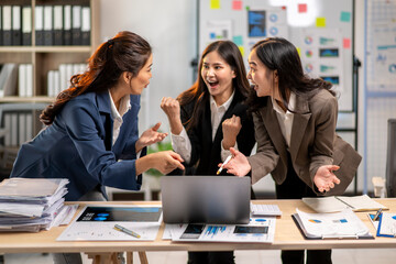 Three women are standing around a table with a laptop open