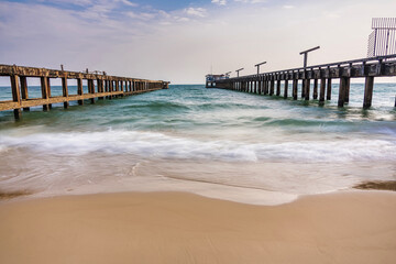 Obraz premium Rustic parallel piers stretch out into the ocean with gentle waves washing onto the sandy beach under a partly cloudy sky