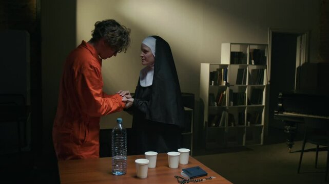 Nun speaking with young inmate holding his hands, then she drinking water from plastic cup when suddenly man grabbing her by throat and pulling to floor