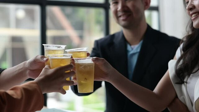 A group of people are holding up plastic cups of beer and smiling. Scene is happy and celebratory