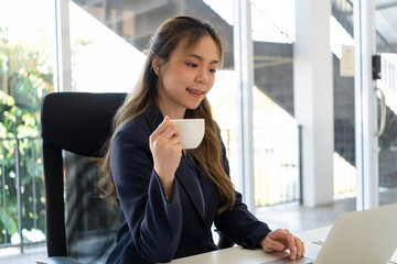 Obraz premium Businesswoman sitting at desk on couch in workplace or at home working on laptop and analyzing data on charts and graphs and writing on papers to make business plan and strategies for company.