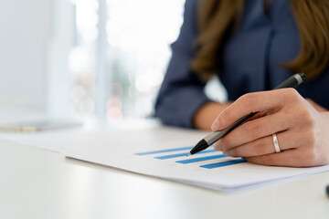 Businesswoman sitting at desk on couch in workplace or at home working on laptop and analyzing data on charts and graphs and writing on papers to make business plan and strategies for company.
