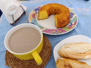 Café-da-manhã com bolo de milho, café com leite e pão francês.