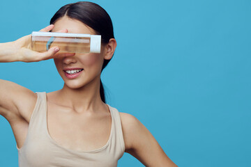 A cheerful young woman of Asian descent playfully holds a transparent container while posing...