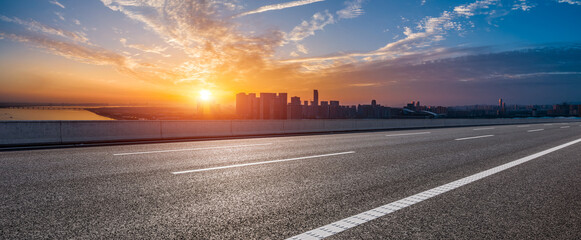 Empty asphalt road with the cityscape at sunrise