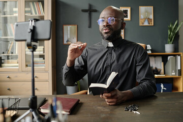 Young African American priest gesticulating in air while having online bible study in office