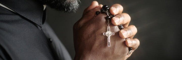 Website banner of unrecognizable pastor holding beautiful rosary with silver cross while praying