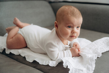 Lying down. Cute little baby is on the sofa