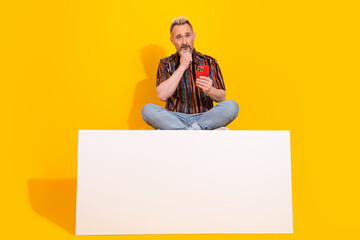 Middle aged man with a modern blond dyed hairstyle posing casually holding a phone against a...