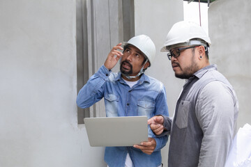 Hispanic engineer man wearing safety white helmet consult team project manager partnership, Asian foreman standing in construction site outdoor fixing error checking blueprint and laptop technology