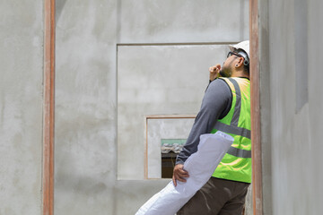Asian overweight construction project foreman inspects construction site holding blueprint...