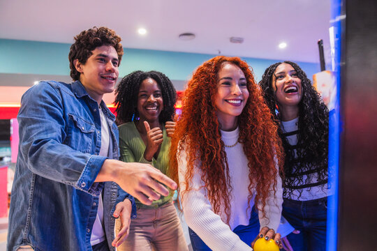 Cheerful young friends enjoying their leisure time, playing arcade games in a vibrant bowling alley - Powered by Adobe