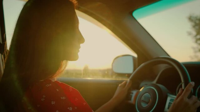 Woman steering car during golden hour, sunlight streaming through window highlighting serene profile. Female driving vehicle with soft evening light, creating warm and peaceful mood inside car. Lady
