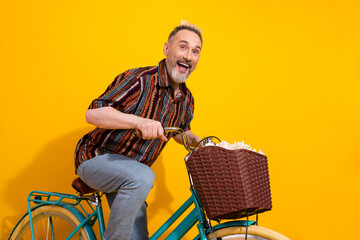 Stylish mature man with dyed blond hair enjoying a fun ride on a retro bicycle with a basket...